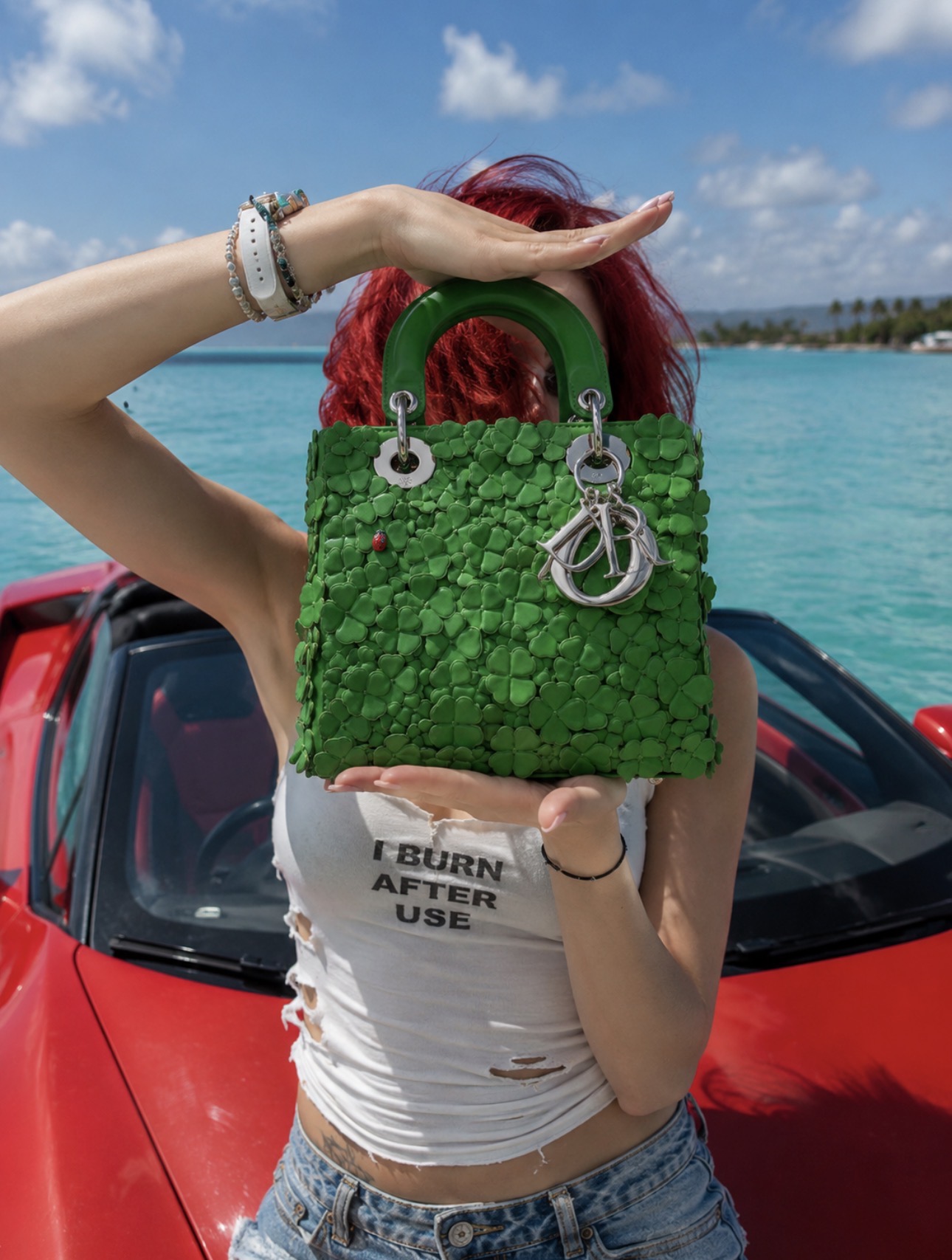 Green designer bag styled near a red car
