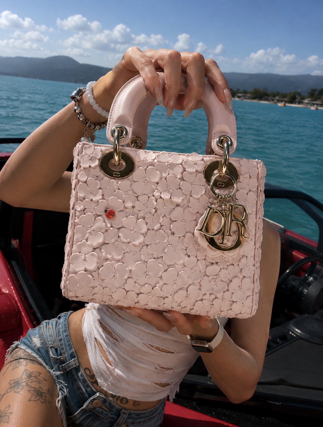 Pink designer bag styled near water and a car